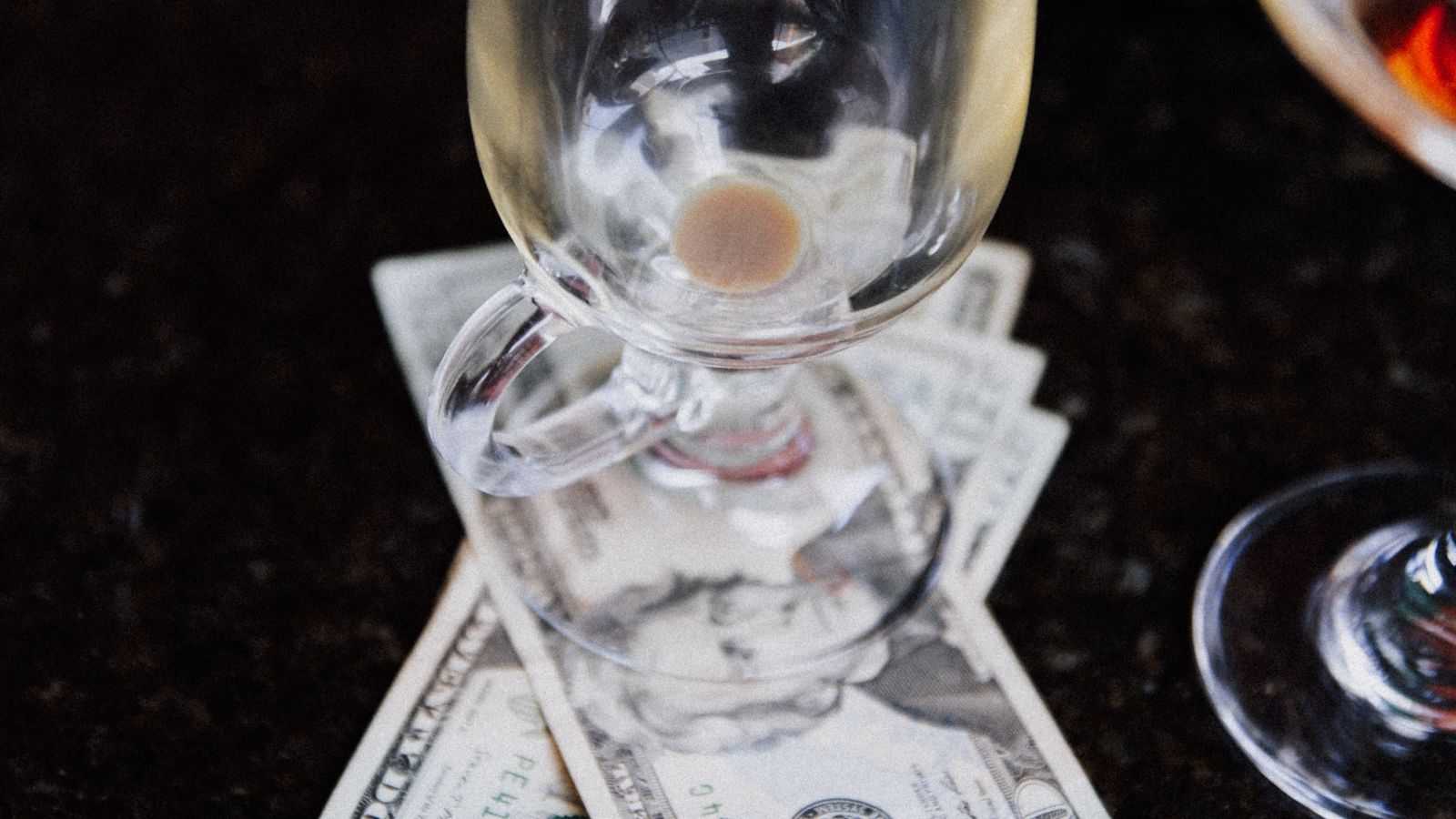 Cash tips left under an empty glass on a bar