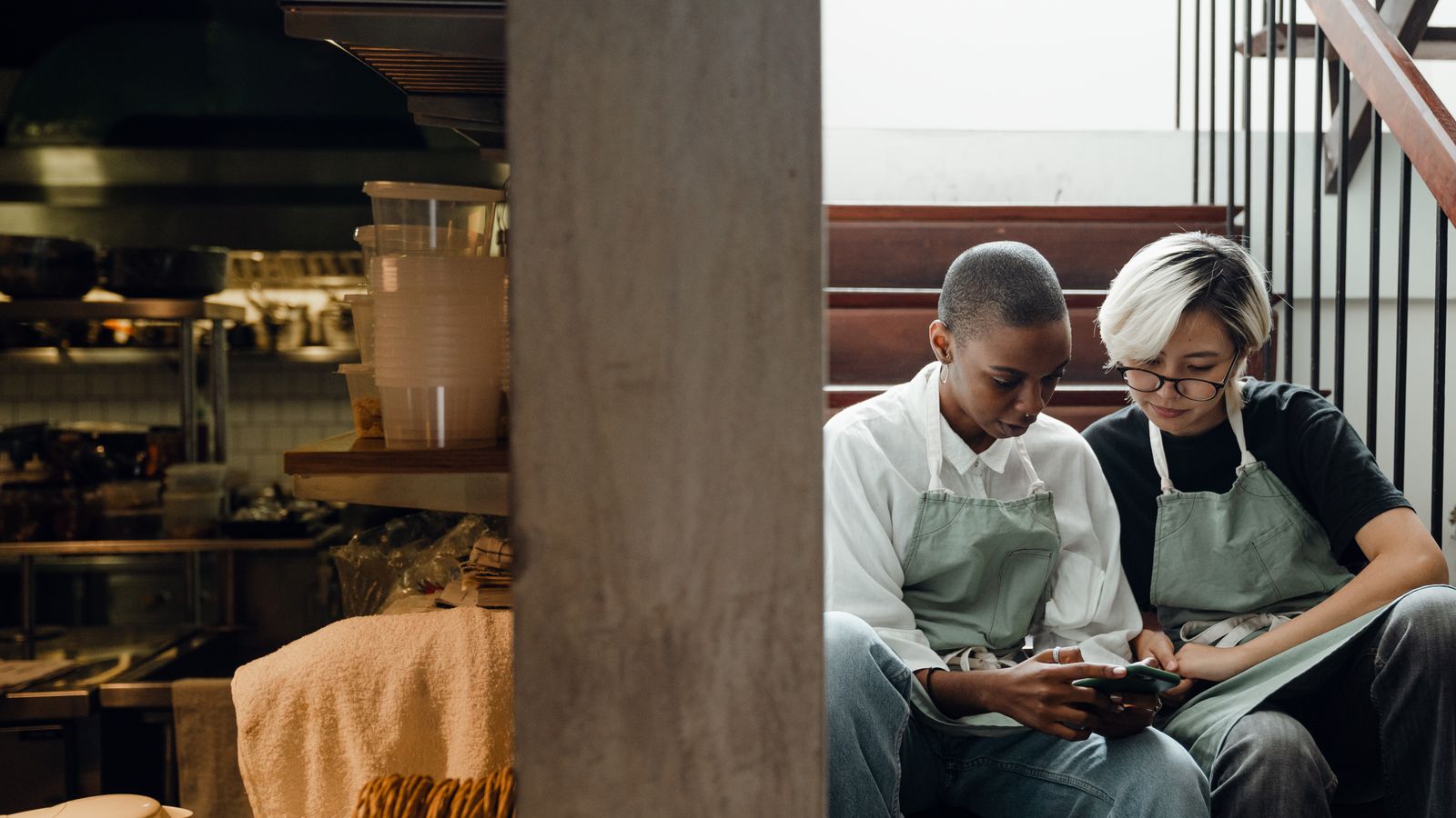 Two restaurant workers in aprons looking at a phone on a break